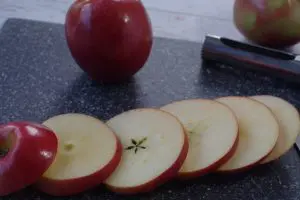 apples, sliced about ¼ inch thick, on a grey cutting board with a whole apple in the background