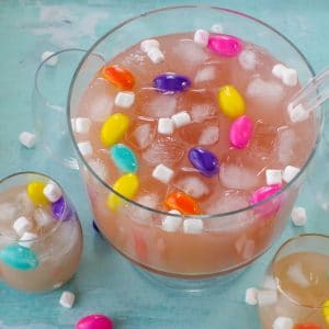 Easter punch in a trifle bowl with glasses around, as well as marshmallow Easter eggs and mini marshmallows