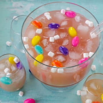 Easter punch in a trifle bowl with glasses around, as well as marshmallow Easter eggs and mini marshmallows