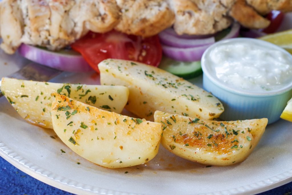 greek style potatoes on a plate with tzatziki and souvlaki