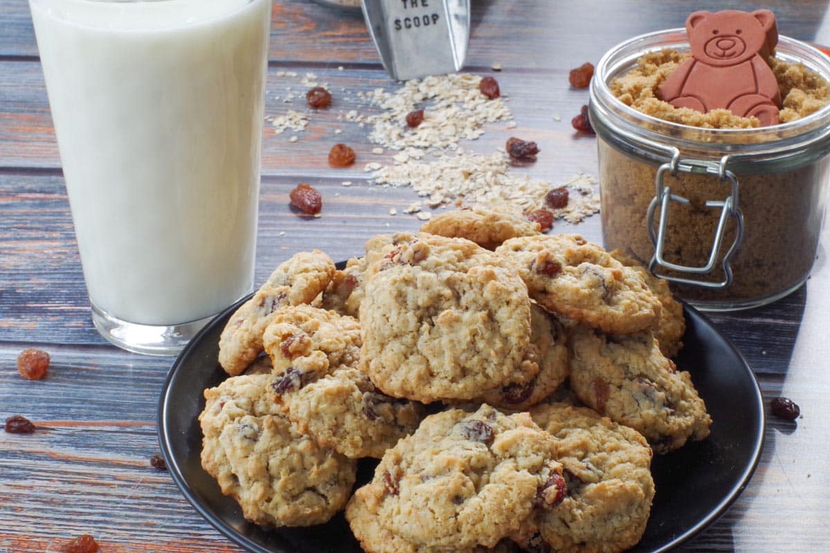 easy oatmeal raisin cookies on a black plate with a glass of milk and a jar of brown sugar in the background