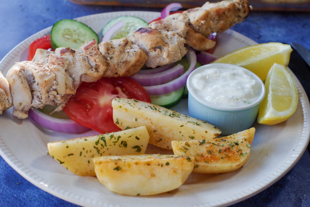 Greek chicken souvlaki on a bed of veggies with greek potatoes, lemon and tzatziki sauce