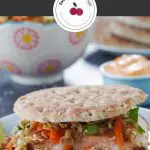 pinterest pin with white text on dark grey background and photo of salmon burger on white plate with coleslaw, buns on a plate and sriracha mayo in background