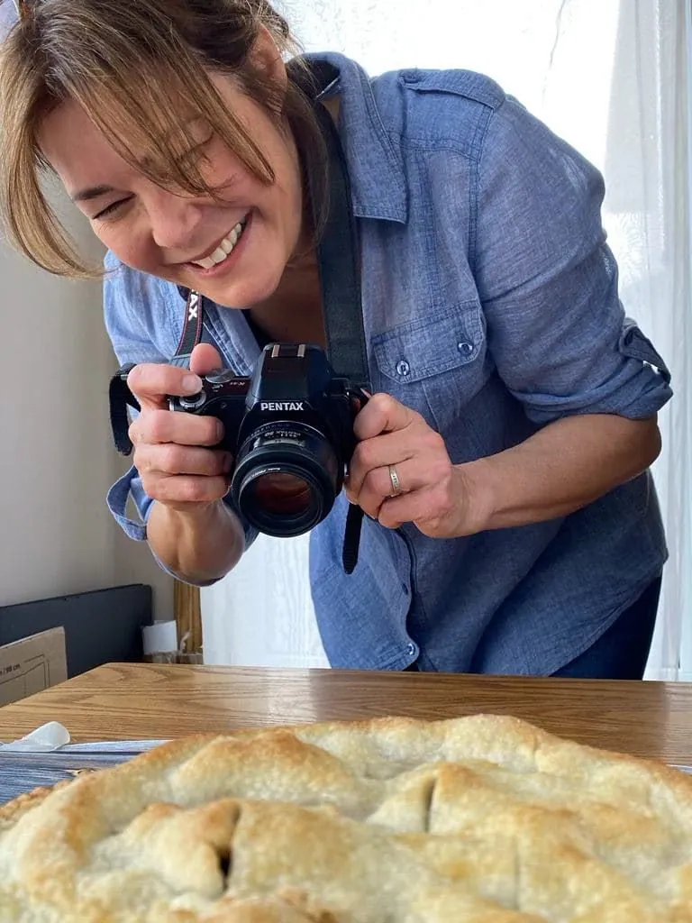 food blogger (me) photographing a pie, holding a camera and smiling