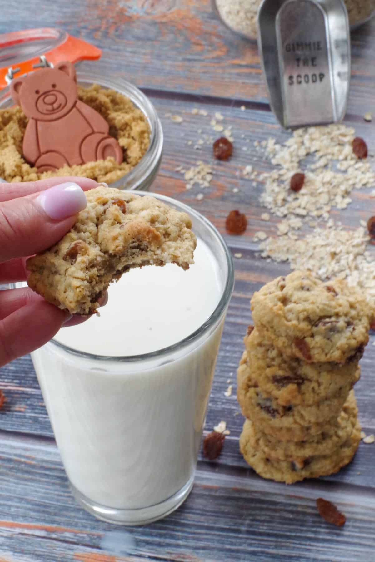 cookie dipped in a large glass of milk, with bite taken out of it, and a large stack of cookies beside milk