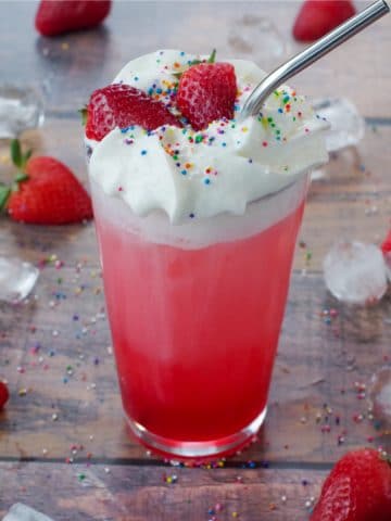 Strawberry Italian Soda in a glass with strawberries, sprinkles and ice surrounding it