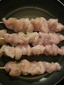 raw skewers in non-stick fry pan