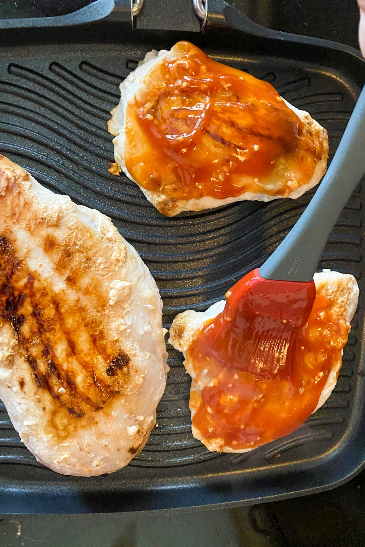 3 pieces of chicken breast on grill with BBQ sauce being spread on one piece