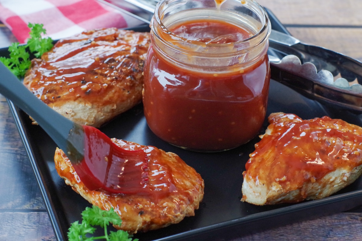 BBQ sauce in middle of black platter with pieces of chicken breast around it