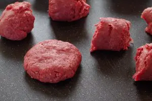 raw ground beef on black cutting board, divided into sections, with one section formed into a patty