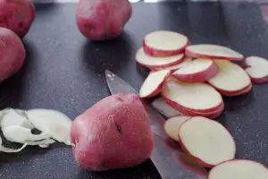 potatoes sliced on cutting board with knife and some onion