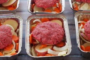 hamburger patties on top of veggies in foil containers