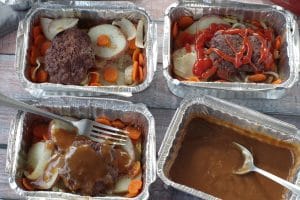 4 hamburger foil packets in aluminum foil containers with potatoes, carrots, onions and hamburgers, on wooden surface