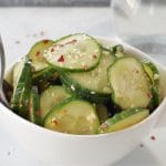 kimchi pickle in white bowl on grey marble counter surface with glass vinegar container in background