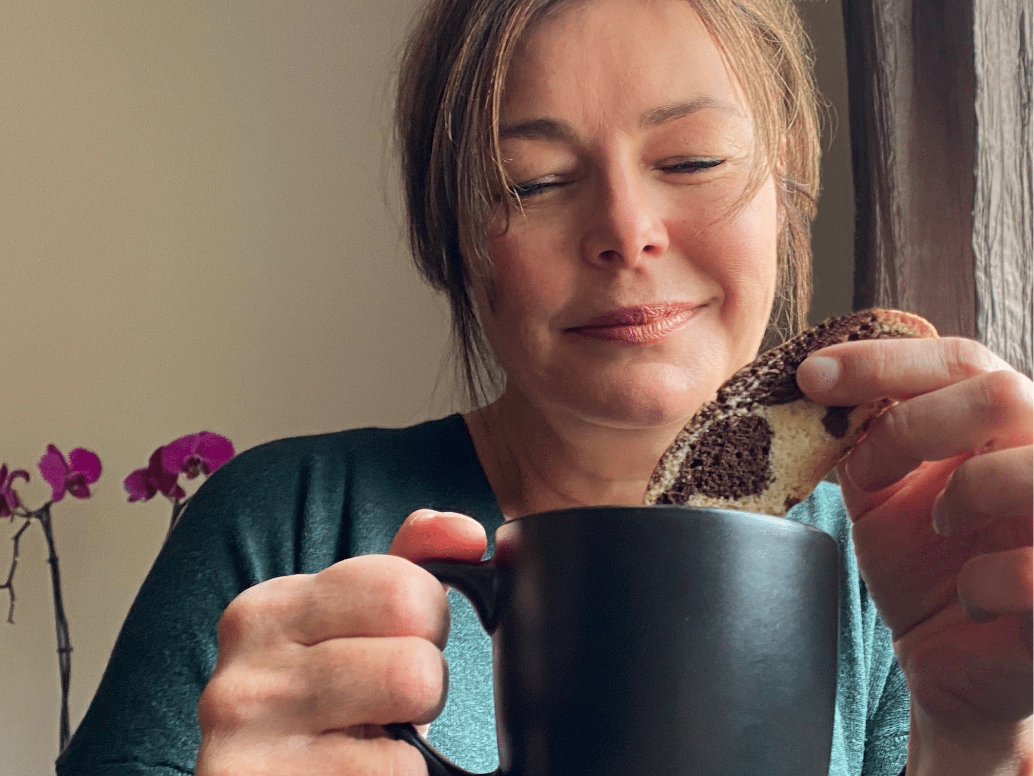 Me, looking down and coffee cup and dunking biscotti into coffee, pink orchid in background