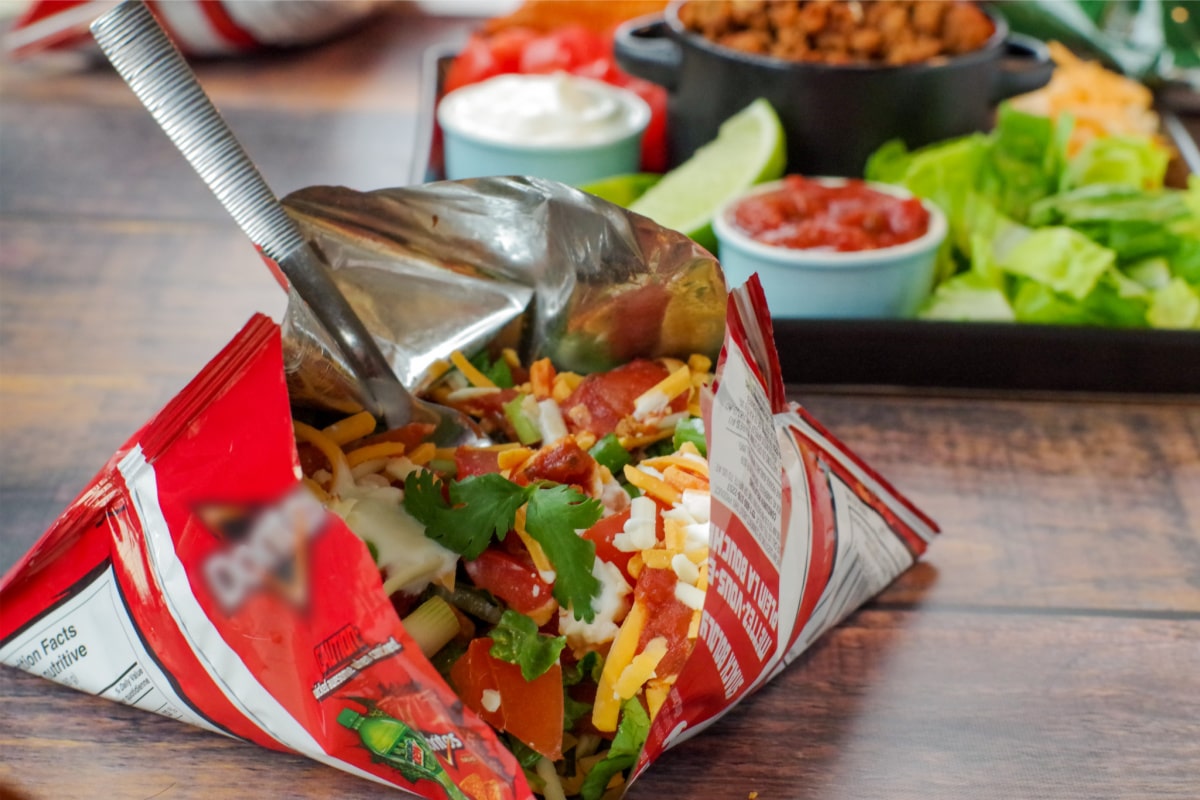 walking tacos in a bag in front and tray of taco meat and fixings in background