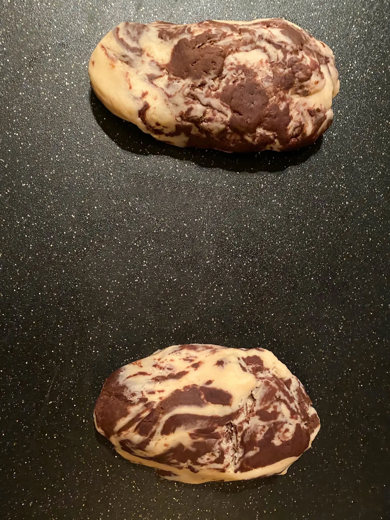 2 portions of marbled biscotti dough on black cutting board