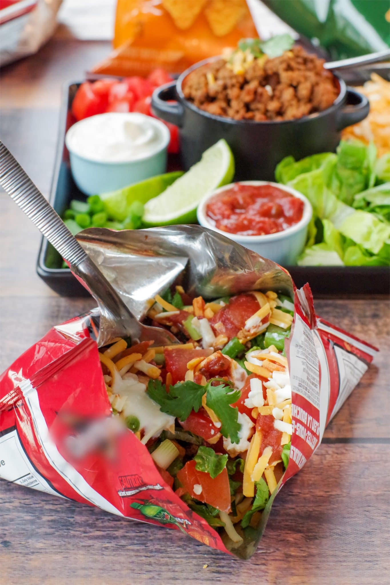 walking tacos in a bag in front and tray of taco meat and fixings in background