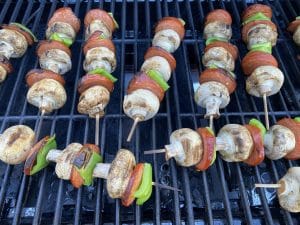grilled pizza toppings (pepperoni, mushrooms and green peppers ) on skewers, on a BBQ grill