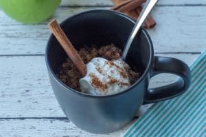 apple crisp in a mug with whipped cream and cinnamon stick