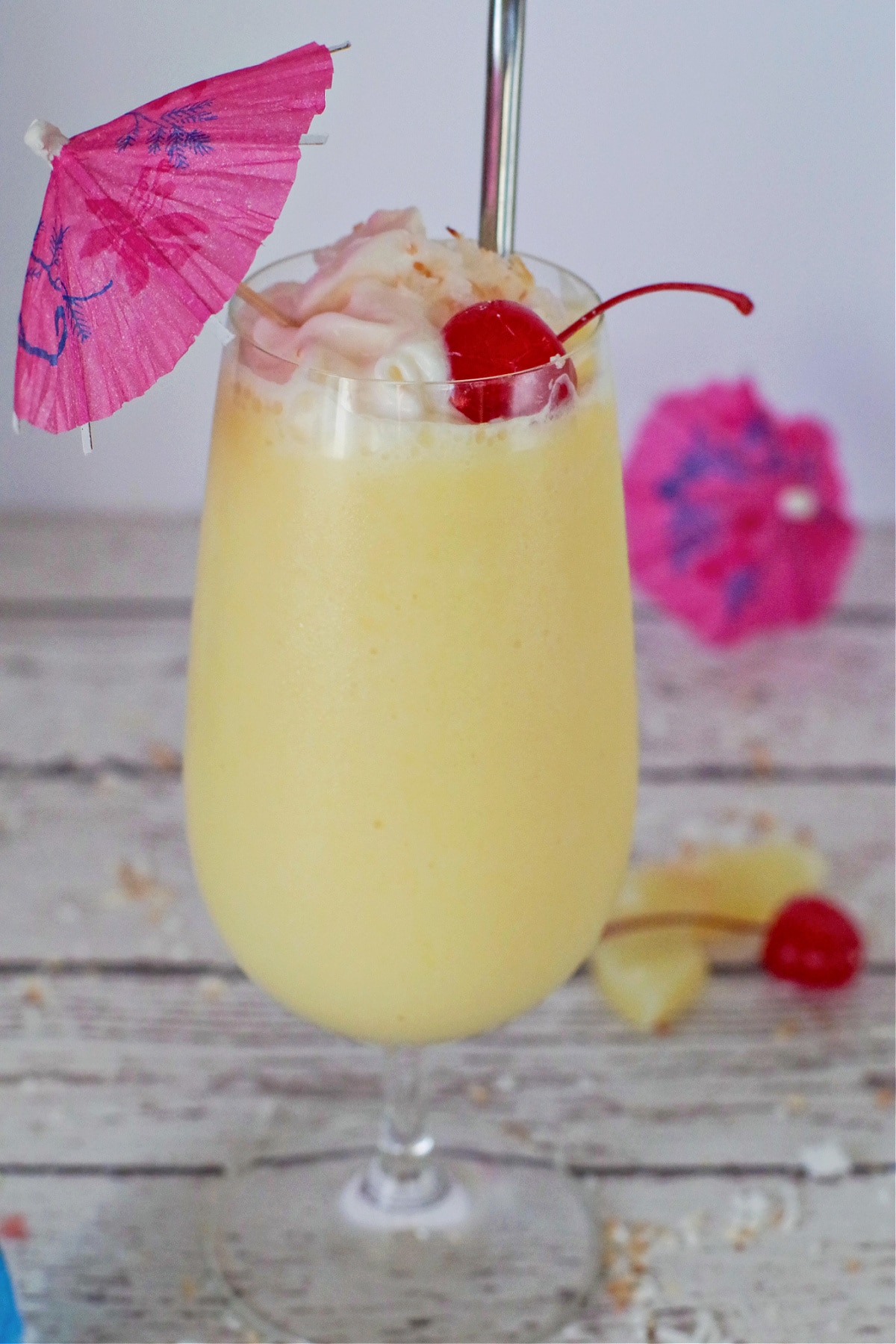  healthy pina colada drink on a white faux wood surface, with pineapple, maraschino cherries and umbrellas