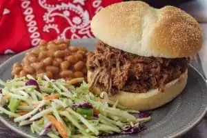 beef on a bun on a grey plate with coleslaw and beans