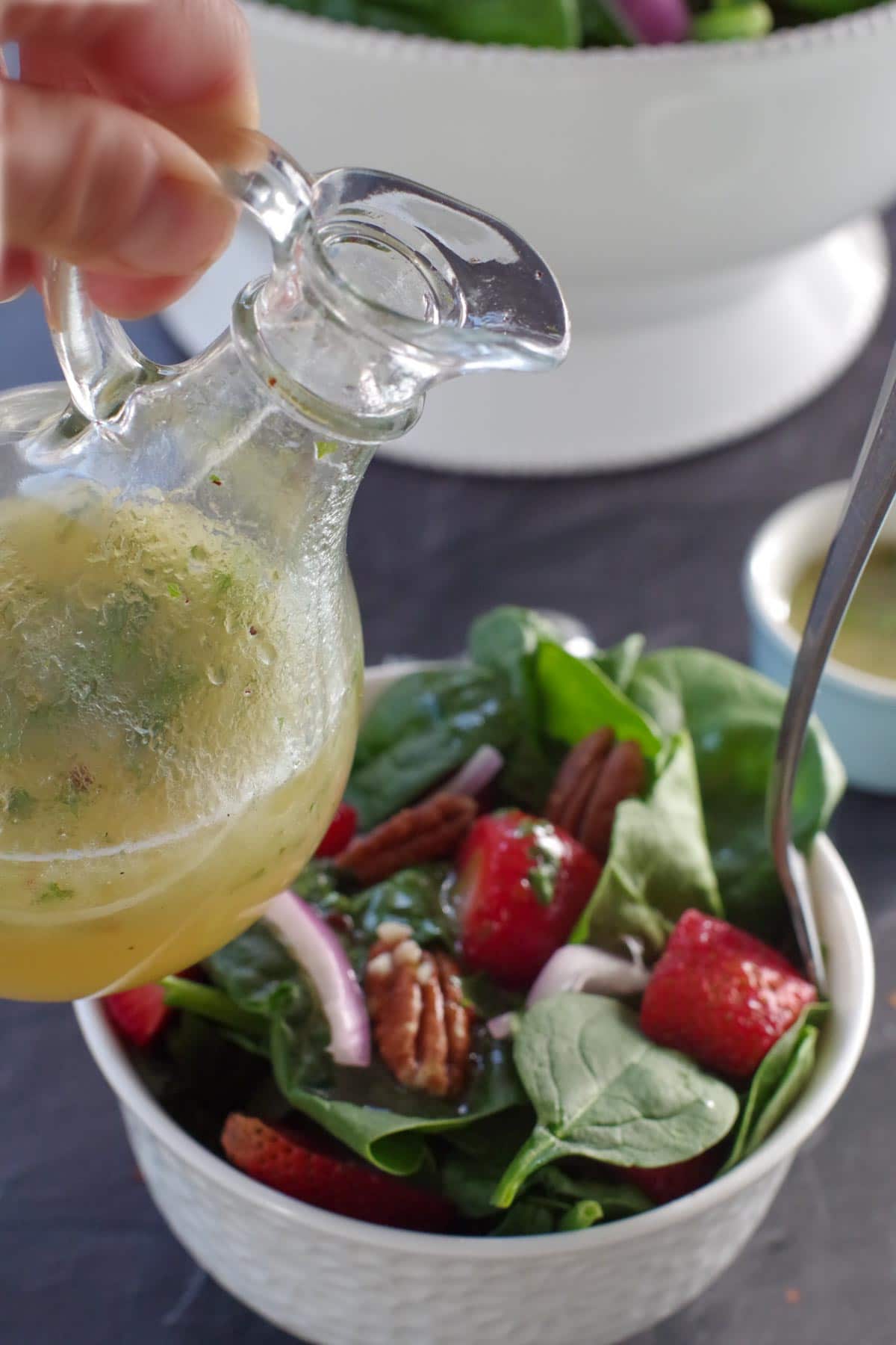 bottle of honey lime cilantro dressing held over a small bowl of strawberry spinach pecan salad