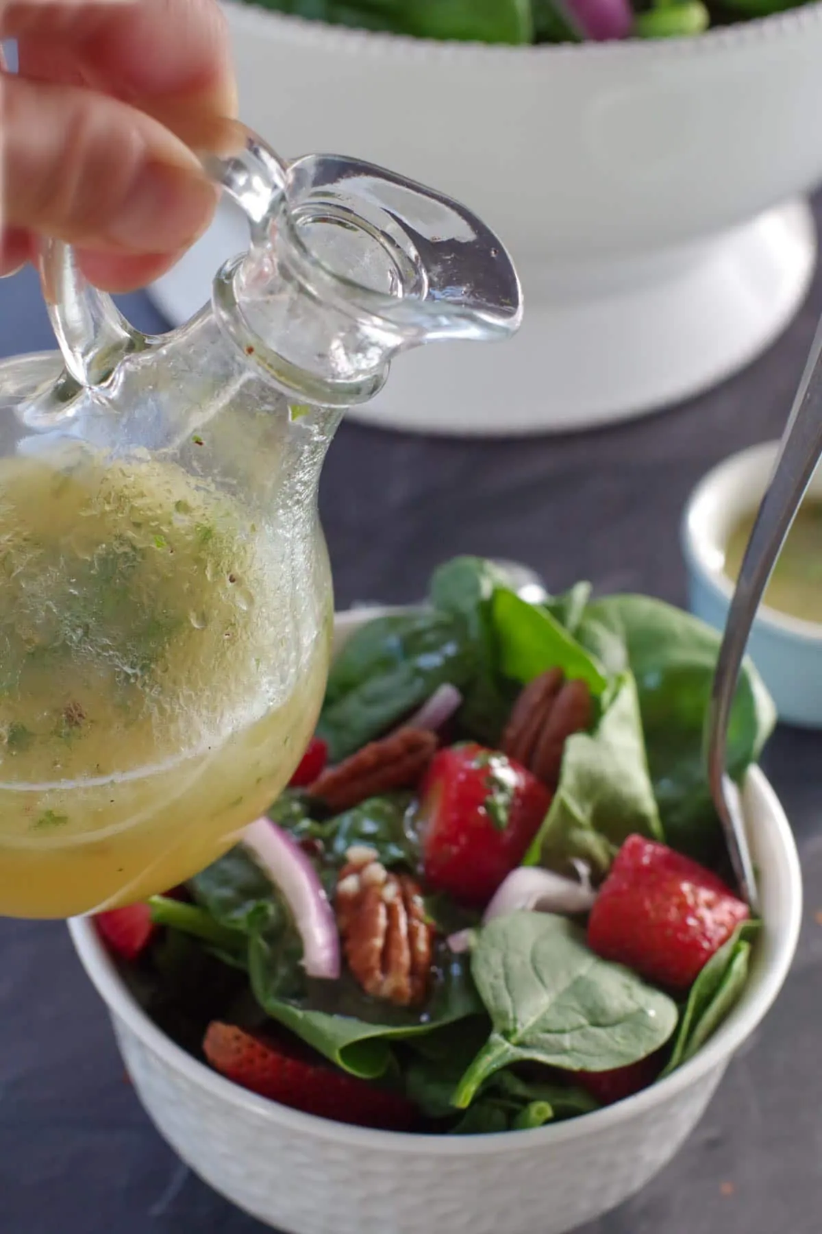 bottle of honey lime cilantro dressing held over a small bowl of strawberry spinach pecan salad