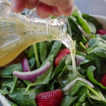 honey lime cilantro vinaigrette being poured over a strawberry spinach salad