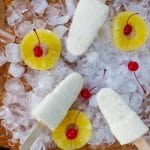 pina colada popsicles on a bed of ice with pineapple and cherries
