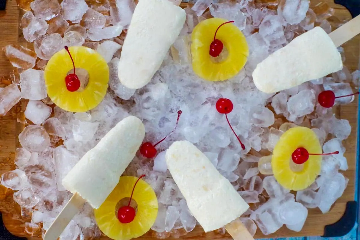 pina colada popsicles on a bed of ice with pineapple and cherries
