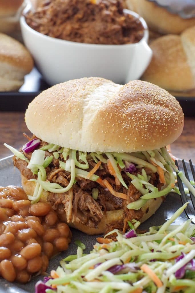 beef on a bun on a grey plate with coleslaw and beans