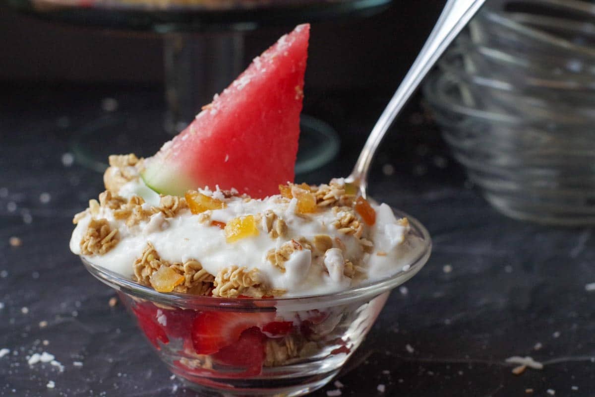 watermelon breakfast parfait in a glass bowl with spoon sticking out and more glass bowls in the backgroun
