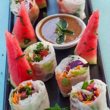 Watermelon Prosciutto Salad rolls, cut in half, on a black platter, with wedges of watermelon
