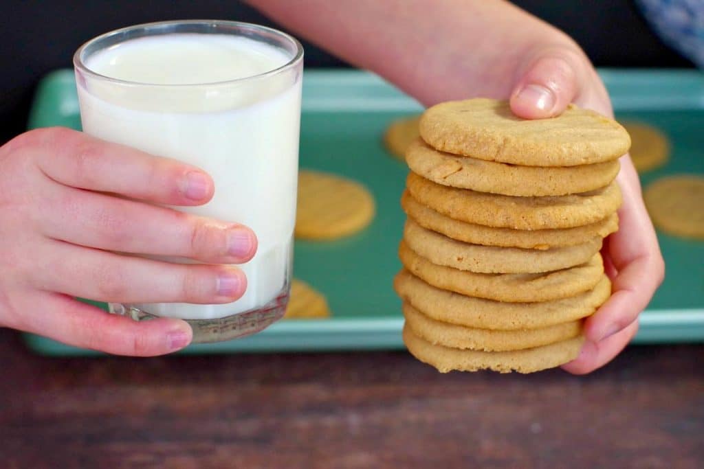hands holding a stack of cookie butter cookie in one hand and a glass of milk in the other
