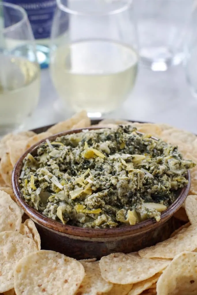 spinach artichoke dip on a platter with glasses of wine in the background