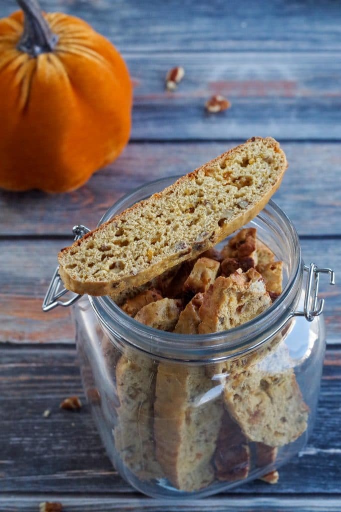 pumpkin biscotti in a glass jar with a piece of biscotti on top and a stuffed pumpkin in the background