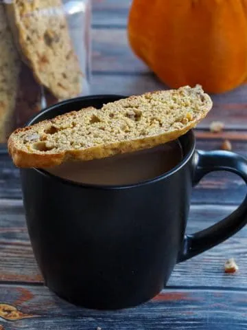 pumpkin spice biscotti on a black mug with a jar of pumpkin biscotti in the background