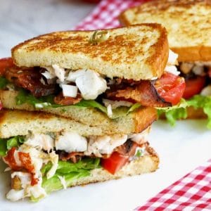 Award-winning lobster BLT. stacked on a white cutting board with red and white checkered napkins