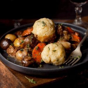 slow cooked beef stew and dumplings in black bowl with a glass ow wine in the background