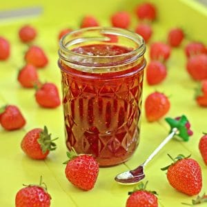 strawberry jam in a jar with strawberries around it on yellow surface