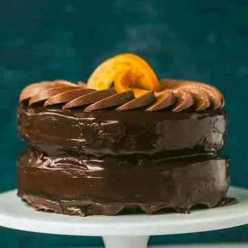 chocolate orange cake on a white stand with dark blue background
