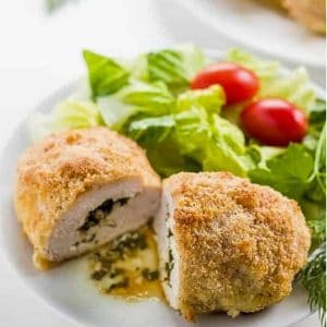 Easy Baked Chicken Kiev. cut in half, on a white plate, with salad