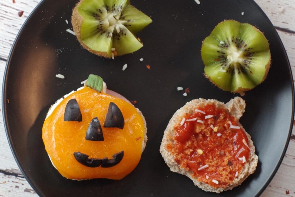 Halloween Breakfast Pizza Sandwich cut into a jack o'lantern on a black plate with kiwi flowers