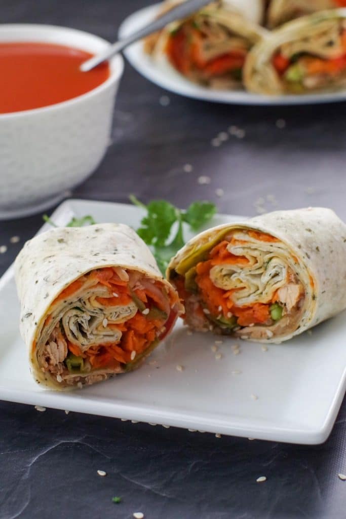 healthy leftover turkey wrap, sliced in half, on white plate, with bowl of tomato soup and platter of turkey wraps in the background