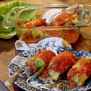 Low carb cabbage rolls on a plate with a glass dish of more of them in the background
