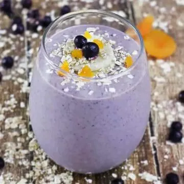 oatmeal and blueberry smoothie in glass on wooden surface, with sprinklings of ingredients around it