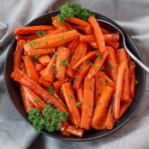 brown sugar glazed carrots in a black bowl, with a spoon, on grey linen