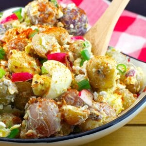 Pierogi Potato salad in a Ukrainian print dish with wooden spoon and checkered red and white towel in the background