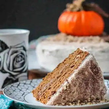 slice of pumpkin layer cake on a white plate with pumpkin in the background